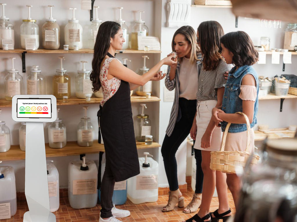 Kiosk NFC/QR do zbierania opinii w sklepie ekologicznym, umieszczony w widocznym miejscu.