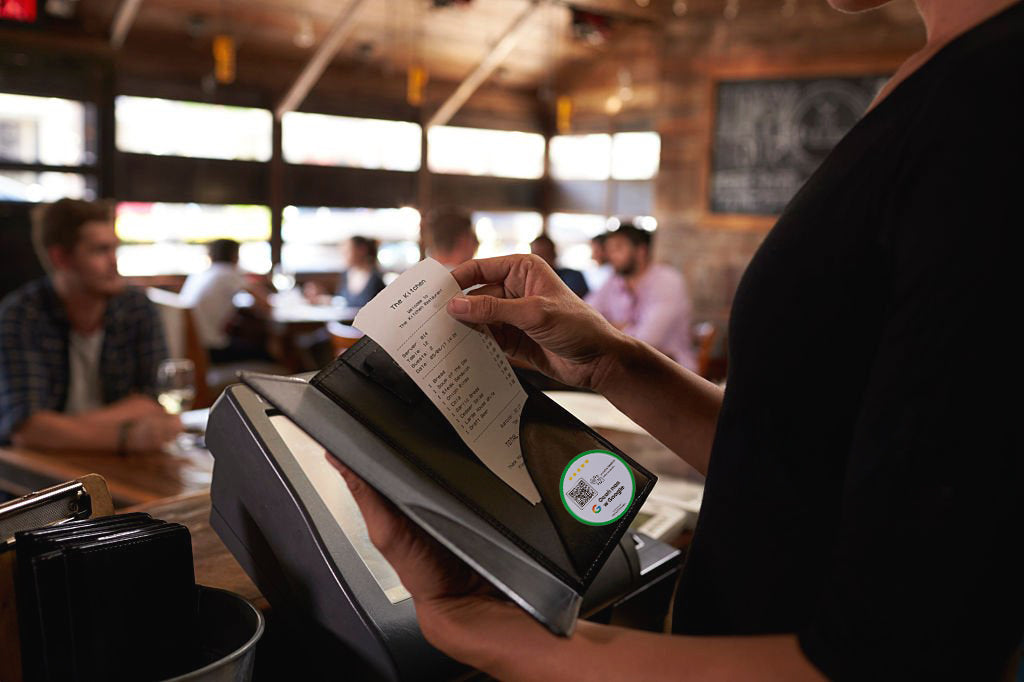 Kelnerka przygotowująca rachunek z naklejką NFC i QR w książeczce